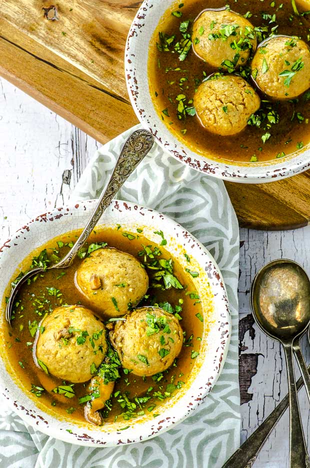 Bird's eye view of a white bowl of vegetarian matzah ball soup in a deep rich colored golden broth. One of our vegetarian Passover recipes.