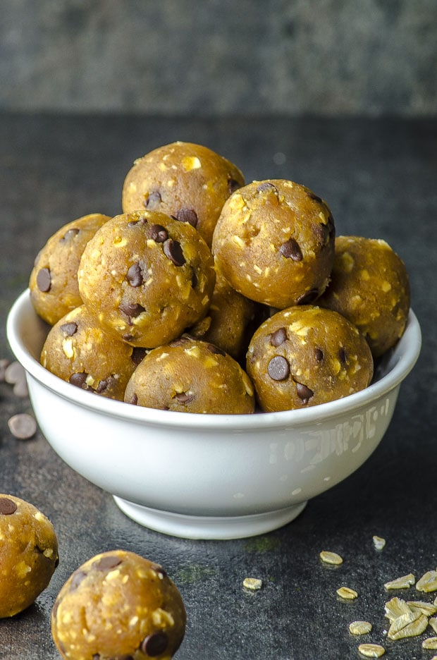 a pile of chocolate chip chickpea cookies dough balls on a white bowl and placed on a black surface