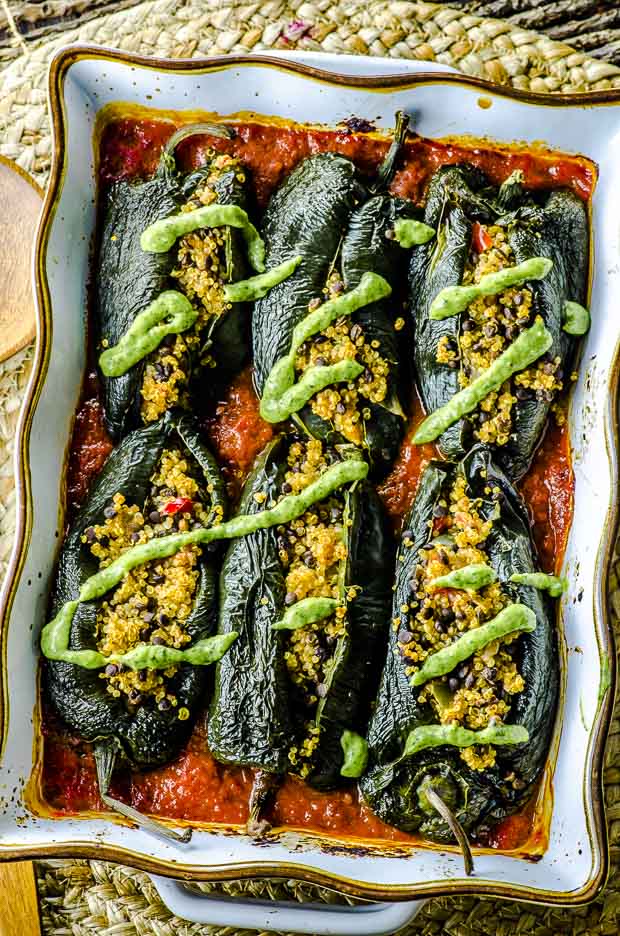 Birds eye view of stuffed poblano peppers with a drizzle of avocado cilantro cream over tomato sauce in a gold rimmed white baking dish 