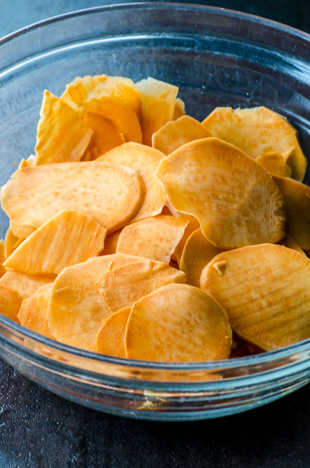 Sweet potato slices in a clear bowl on a dark blue surface
