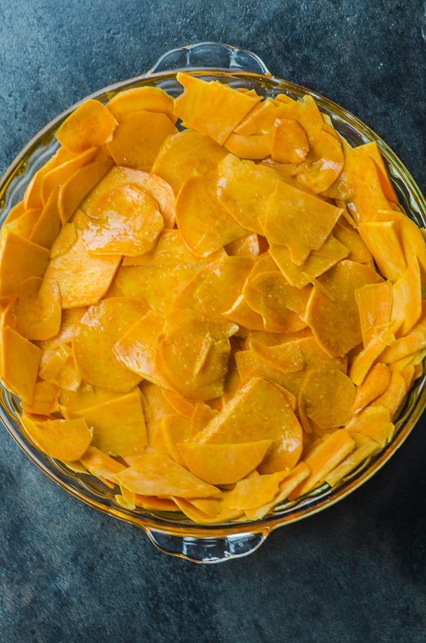 Sweet potato slices arranged on a clear round baking dish, on a dark blue surface