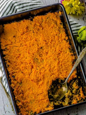 Birds eye view of the Sweet Potato Shepherd's Pie with a silver spoon, on a white an gray striped cloth napkin and a yellow flower on the corner