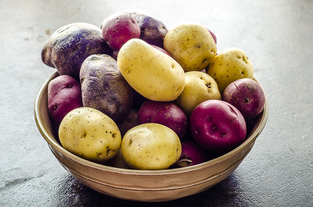 Close up of a small browl bowl filled with raw yellow, red and purple potatoes