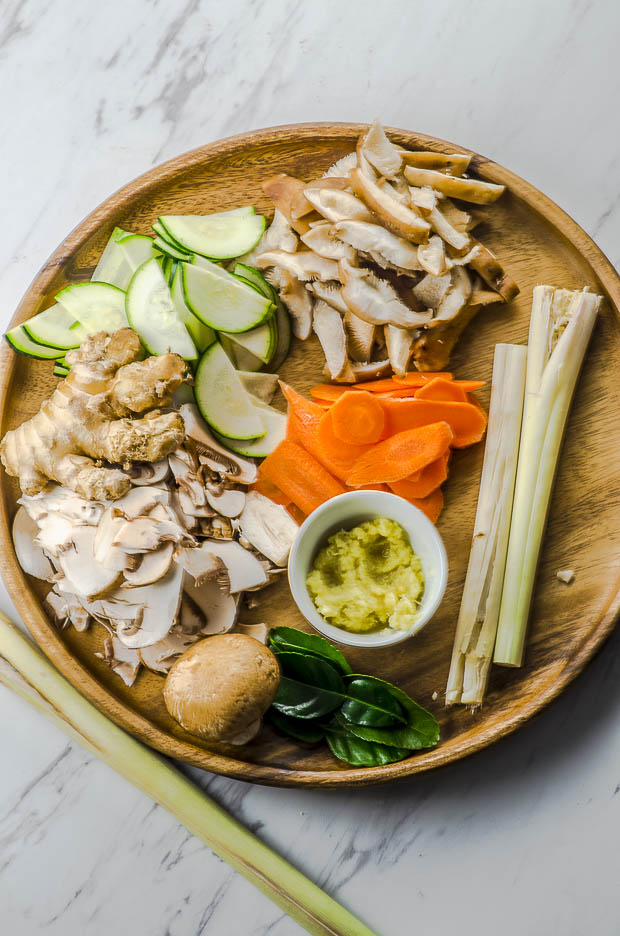 Sliced mushrooms, zucchini and carrots, grated ginger and two lemon grass stalks on a round wooden board