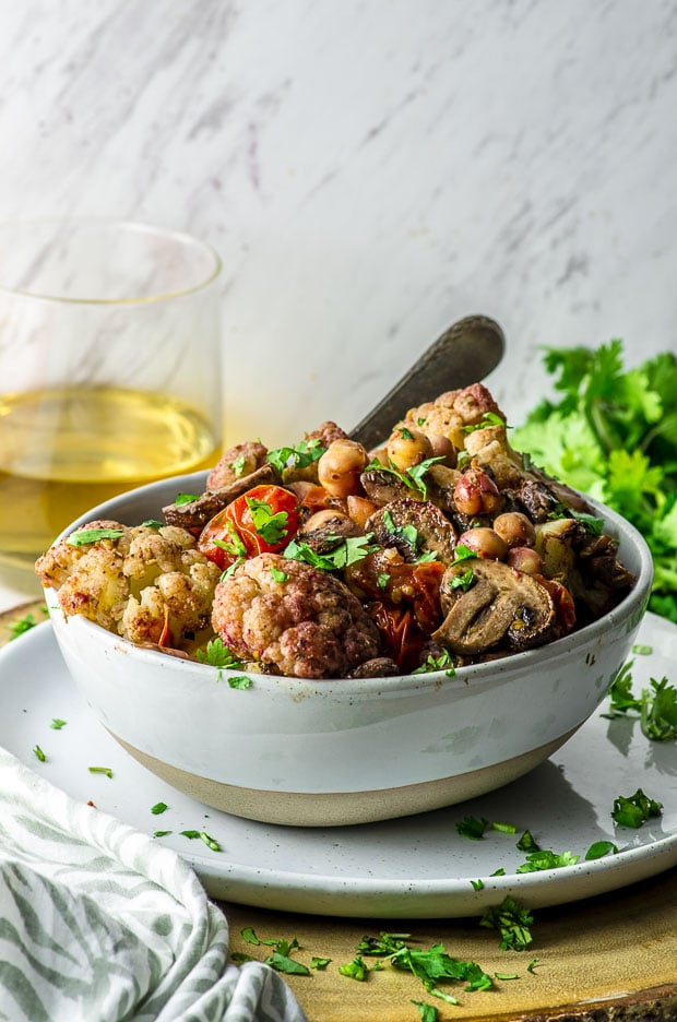 Cauliflower Chickpea Sheet Pan Dinner in a white bowl with a serving spoon, and chopped cilantro sprinkled on top and around.