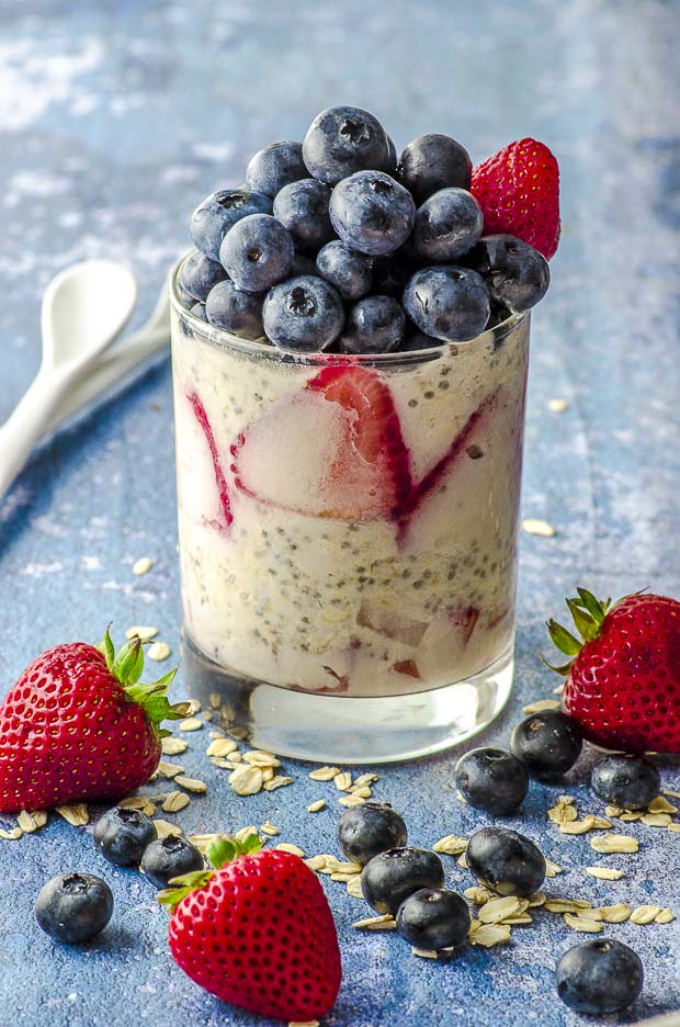 A cup of red white and blue vegan overnight oats, topped with a pile of blueberries