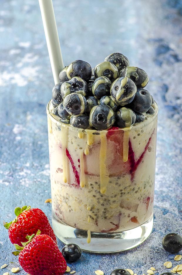 Close up of a cup of red white and blue vegan overnight oats, topped with a pile of blueberries and a drizzle of tahini