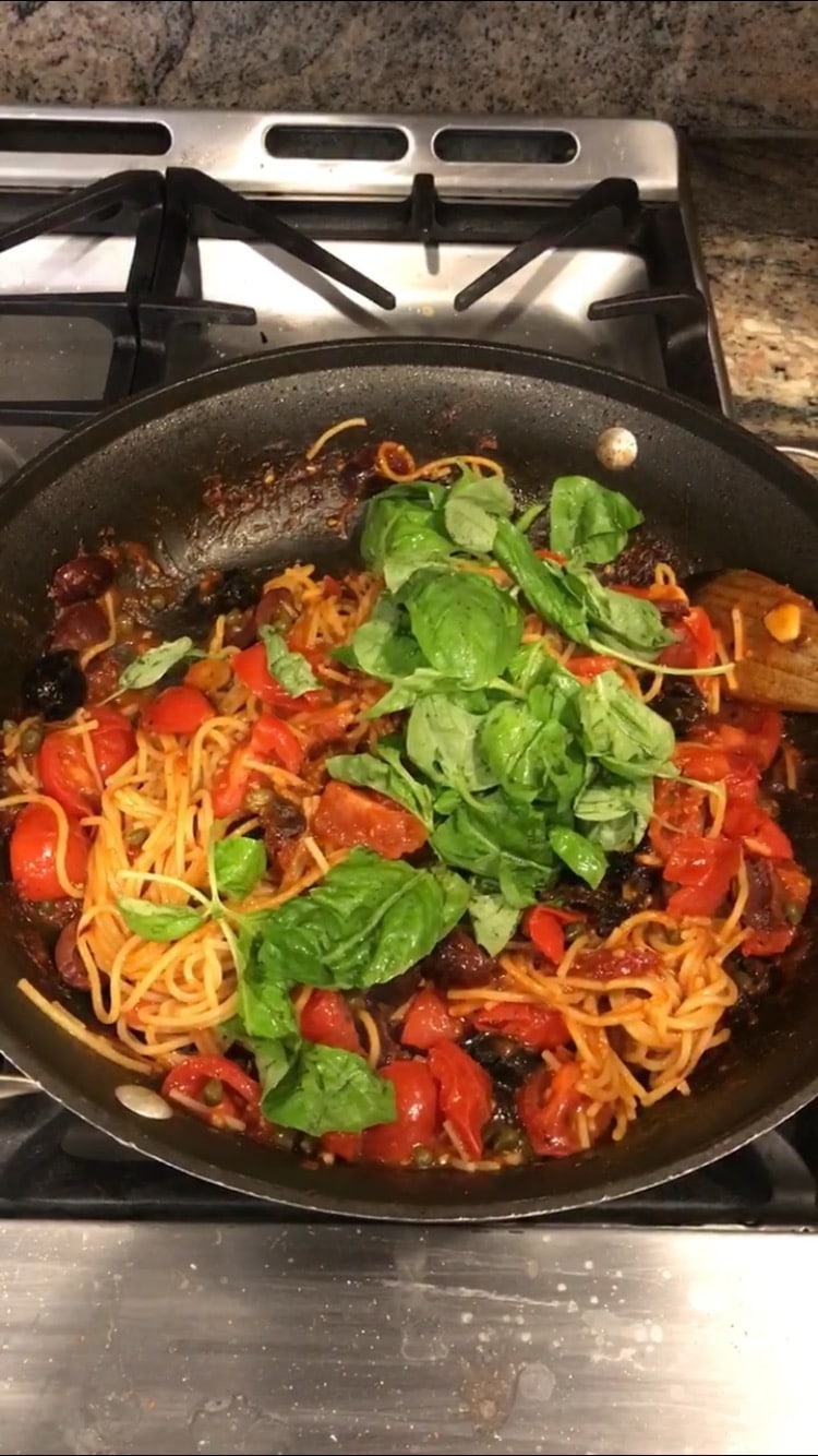 Adding basil to pasta puttanesca cooking in a skillet