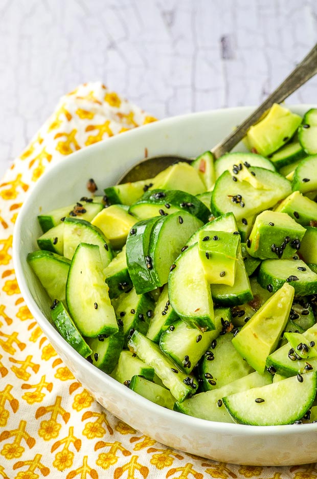 Close up of the avocado cucumber salad in a white bowl, over a white and yellow cloth napkin