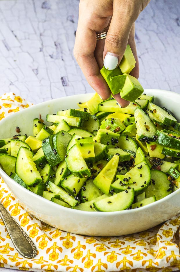 Avocado cucumber salad in a white bowl, with some diced avocado being added to the bowl