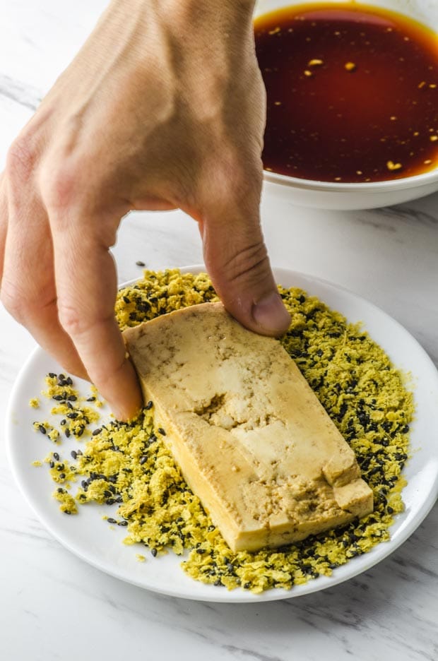 Dipping tofu in nutritional yeast and sesame seeds for a veggie sandwich