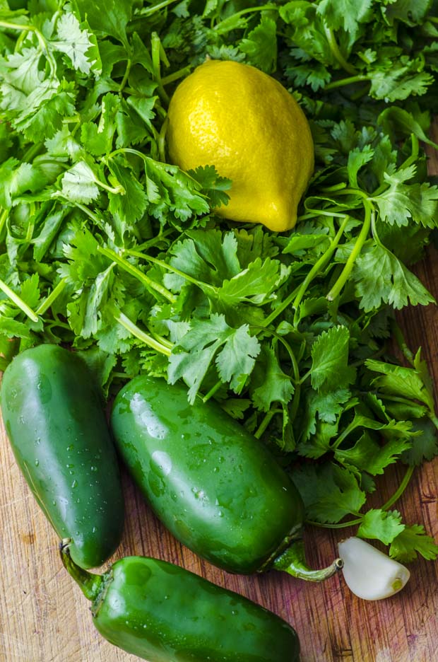 Birds eye view of jalapeno peppers, cilantro, garlic and a lemon on a wooden board