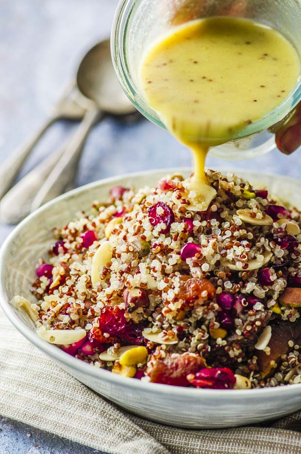 pouring dressing on a bowl of quinoa salad