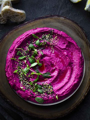 overhead view of a plate with beet hummus topped with sesame seeds and sprouts
