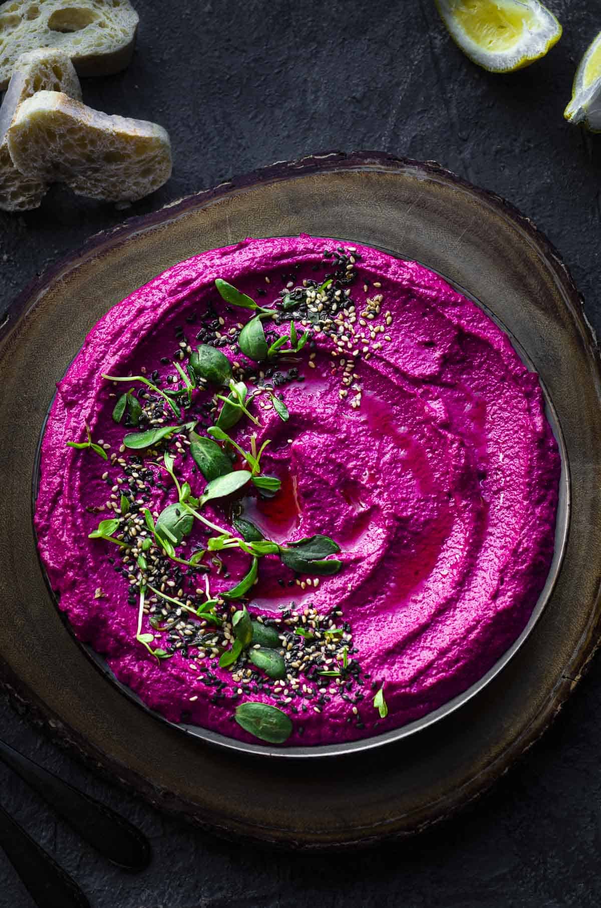 overhead view of a plate with beet hummus topped with sesame seeds and sprouts