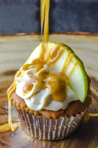 A frosted apple cupcake with a slice of green apple and a drizzle of caramel