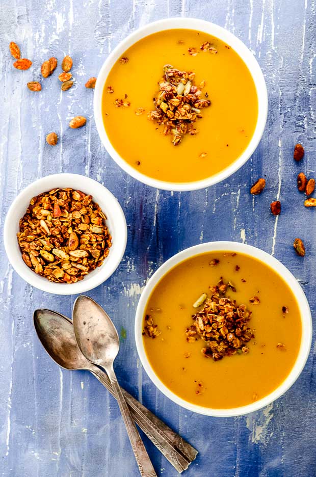 Bird's eye view of two white bowls filled with pumpkin soup and a small bowl filled with savory granola