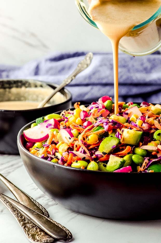 Pouring peanut dressing over a bowl of breakfast salad.