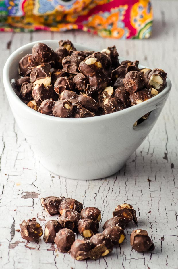 Side View of Chocolate covered roasted hazelnuts in a white bowl.