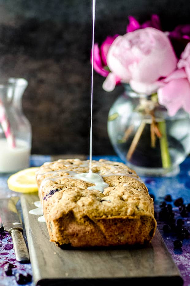 pouring lemon glaze on a lemon blueberry cake