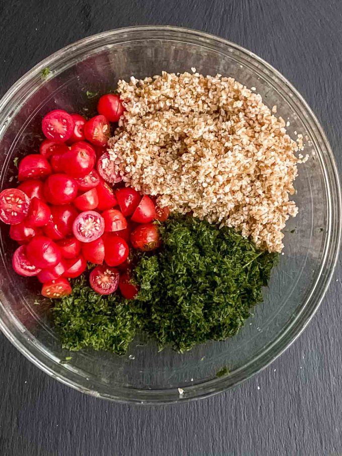 chopped parsley, soaked bulgur wheat and fresh tomatoes in a bowl ready to be mixed for tabouli salad