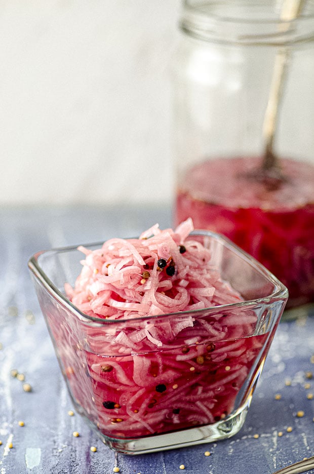 A close up of A Clear bowl filled with pickled onions and a jar of pickled onions in the background.