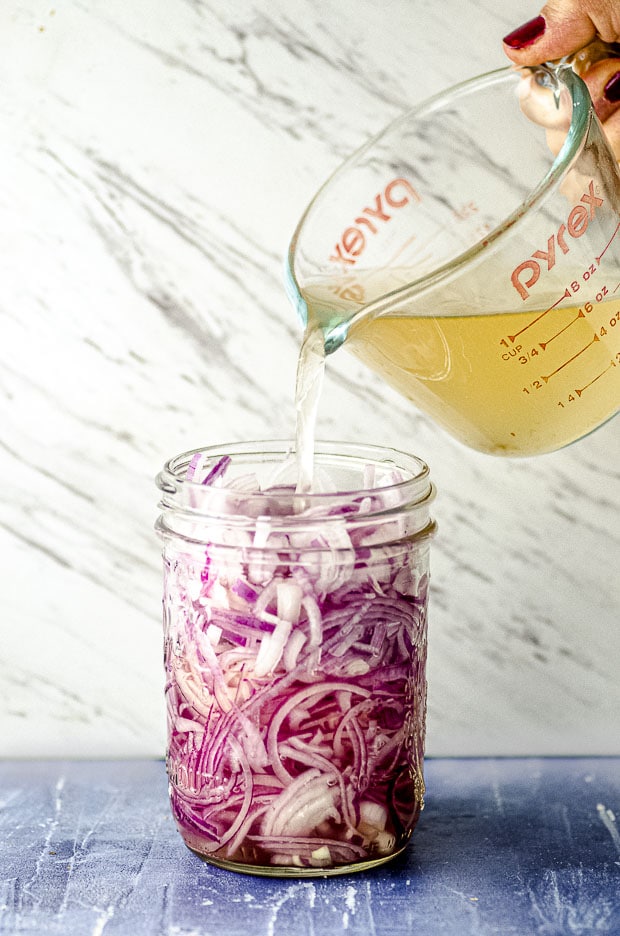 Pouring vinegar, salt and water into a jar or red onions in order to make pickled onions.