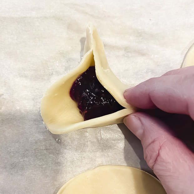 Pinching the bottom sides of the hamantaschen dough