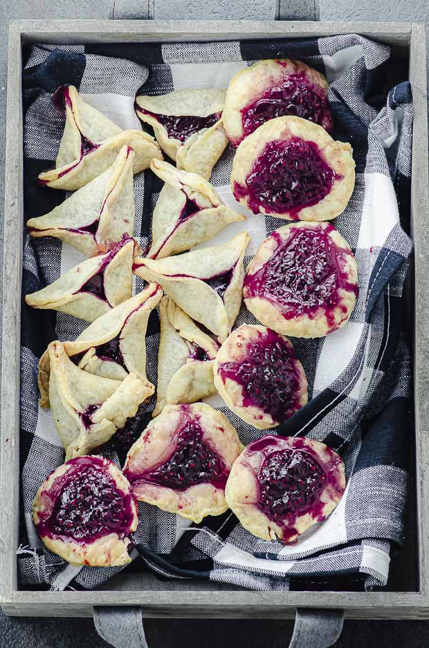 A wood box lined with a black and white napkin filled with raspberry hamantaschen
