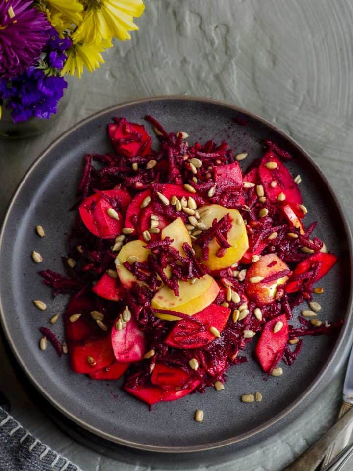 Close up view of of a plate with beet salad topped with sunflower seeds and pickled onions