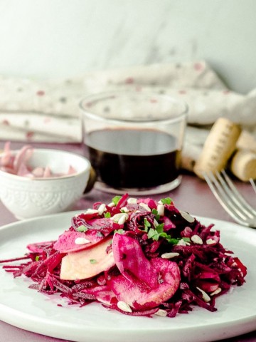 Side view of a plate with raw beet salad topped with sunflower seeds and parsley
