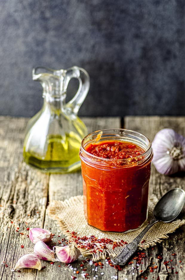 A jar of matbucha with a bottle of olive oil in the background