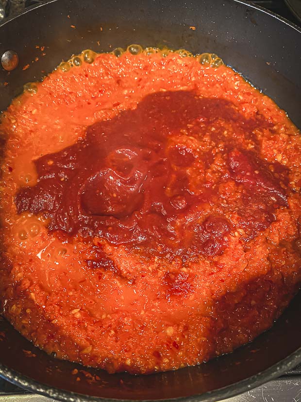 adding crushed tomatoes to a puree of peppers and garlic