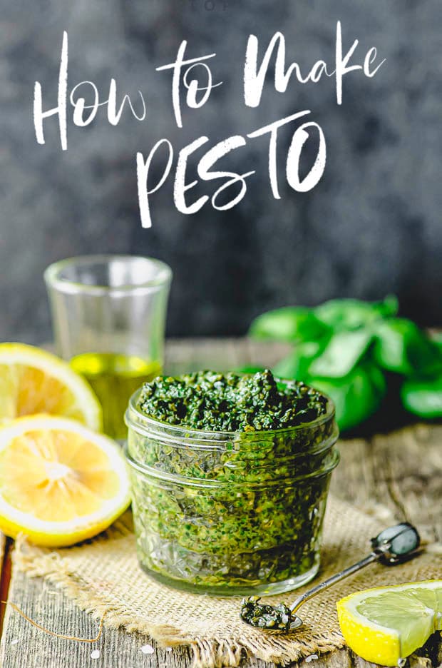 side view of a small mason jar filled with pesto with some lemons and olive oil in the background