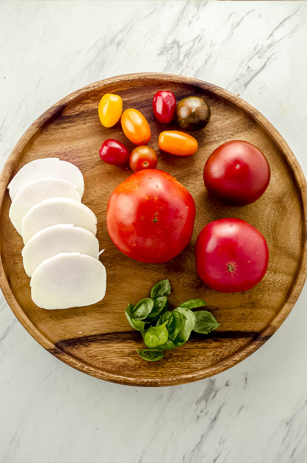 Bird's eye view of a wood plate with the ingredients to make a caprese salad. tomatoes, mozzarella cheese and basil