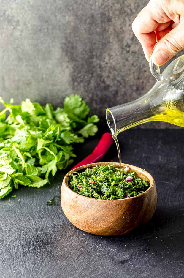 Pouring oil on a wood bowl of Chimichurri