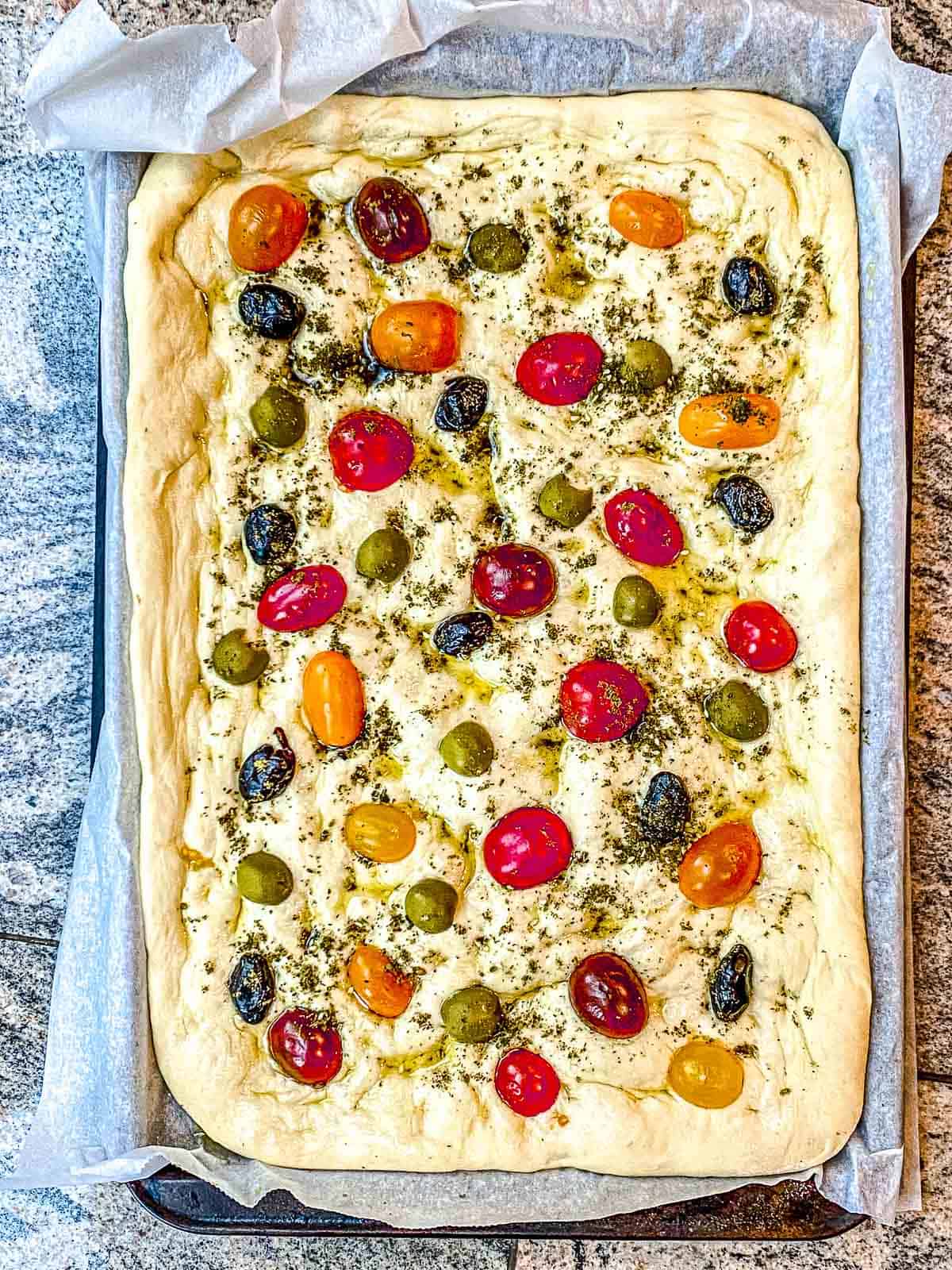 Focaccia bread dough with all of the toppings on top ready to be placed in the oven