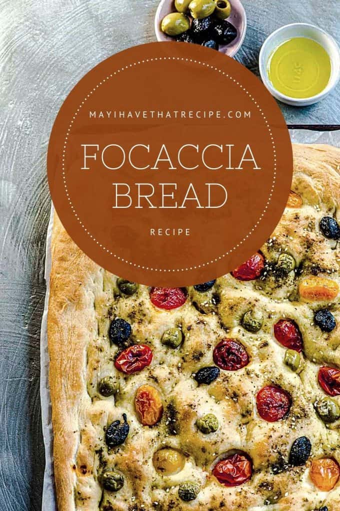 The corner side of a whole focaccia bread with two little bowls of oil and olives