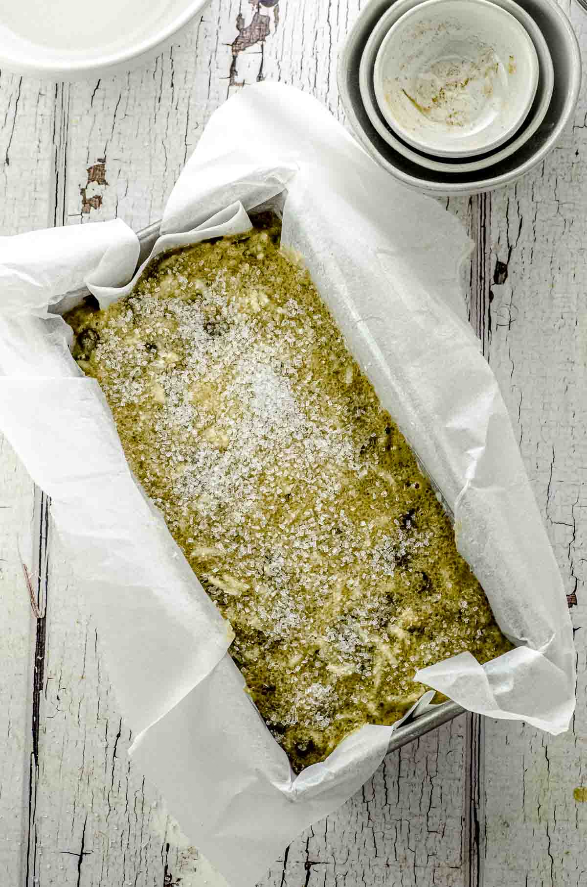 Overhead view of a loaf pan lined with parchment paper filled with batter and sparkling sugar on top ready to be baked