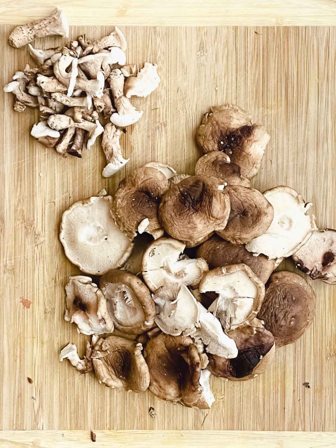 Shiitake mushrooms on a wood cutting board with the caps and stems separated