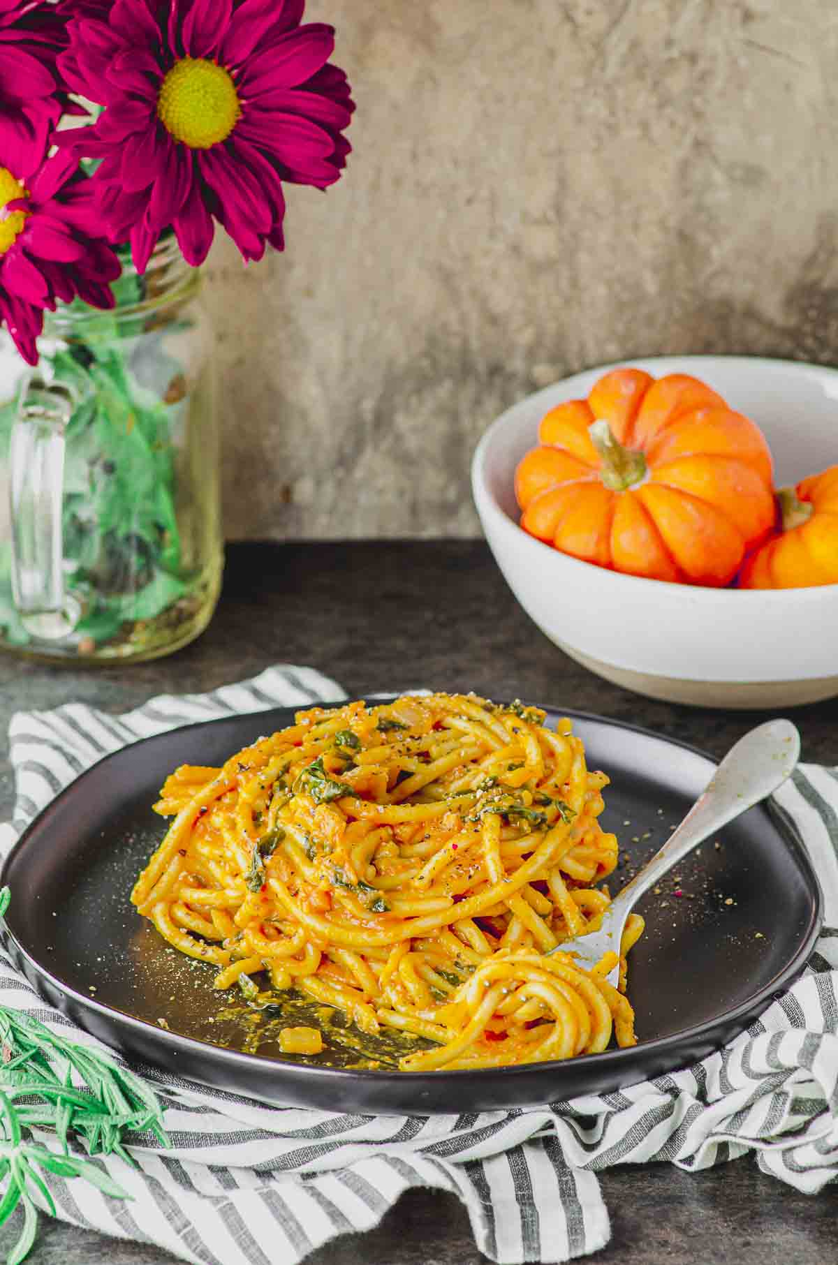 Side view of a plate of spaghetti with pumpkin pasta sauce and a bowl with mini pumpkins on the background