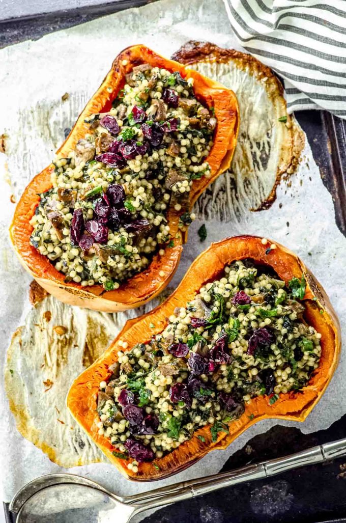 Overhead view of two roasted butternut squash halves stuffed with Israeli couscous and topped with dried cranberries