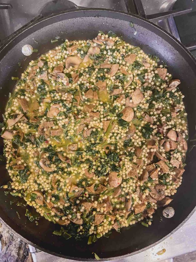 Adding water to Israeli couscous to mushrooms, sausage and spinach