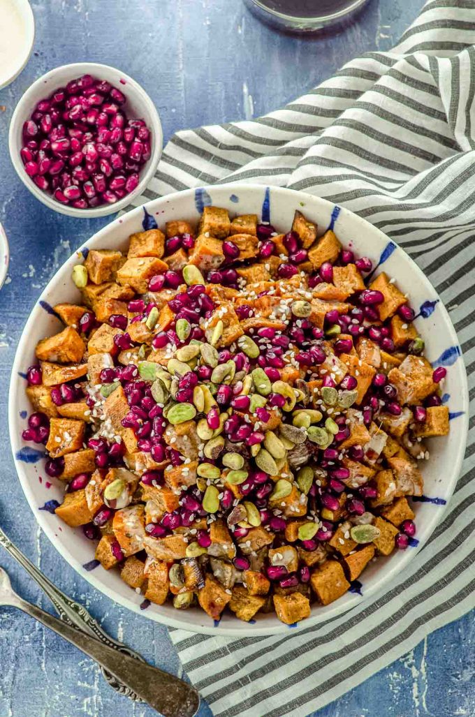 Close up Bird's eye view of a bowl filled with roasted sweet potato cubes topped with Tahini, silan, pistachios and pomegrantes