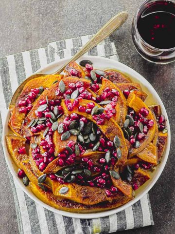 overhead view of a white plate filled with roasted pumpkin and topped with pumpkin seeds and pomegranates seeds