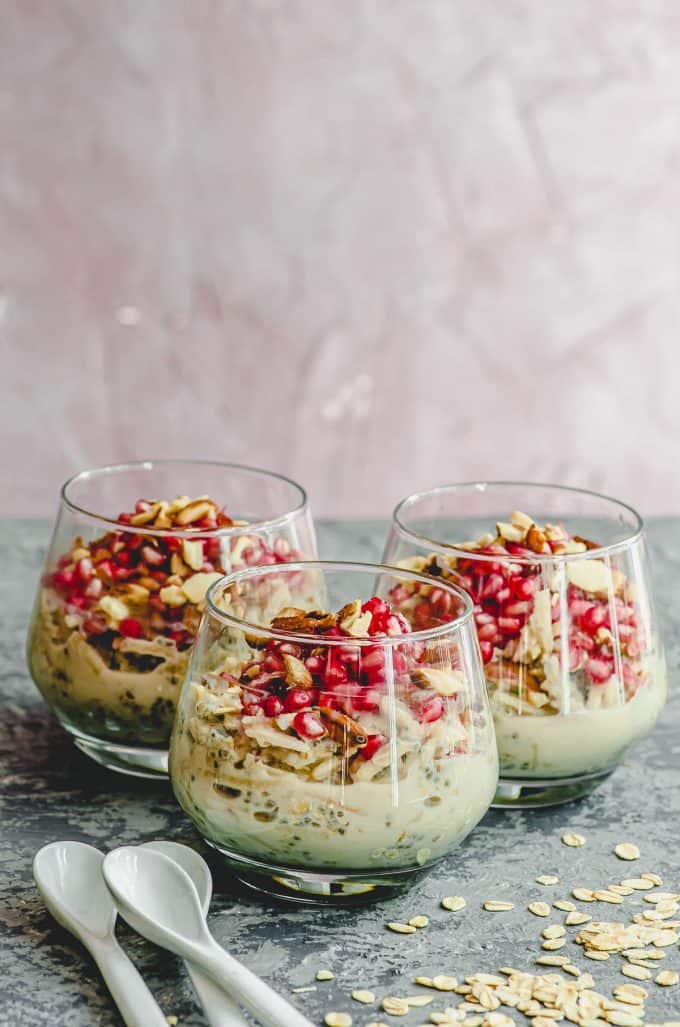 side view of 3 clear cups with overnight oats topped with pomegranates and almonds