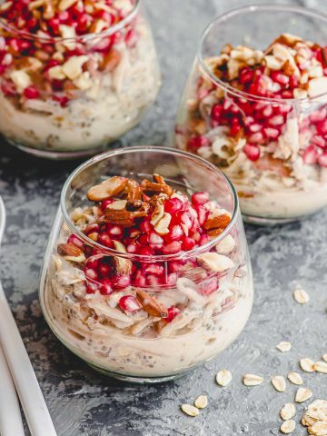 45 degree angle view of 3 clear cups with overnight oats topped with pomegranates and almonds