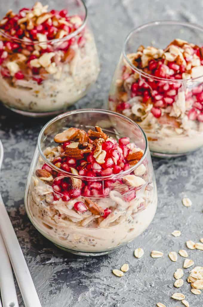 45 degree angle view of 3 clear cups with overnight oats topped with pomegranates and almonds
