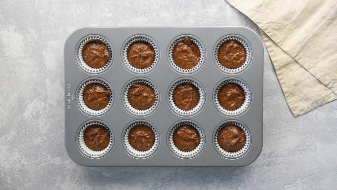 A cupcake pan with liners filled with vegan chocolate cupcake batter