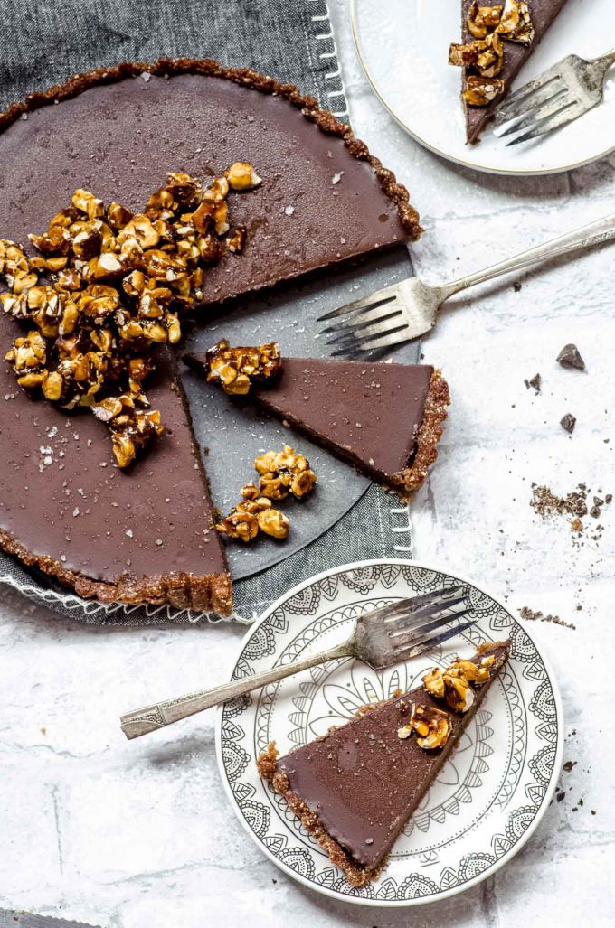 A Chocolate tart with a crunchy roasted hazelnut topping next to two plates with two tart slices